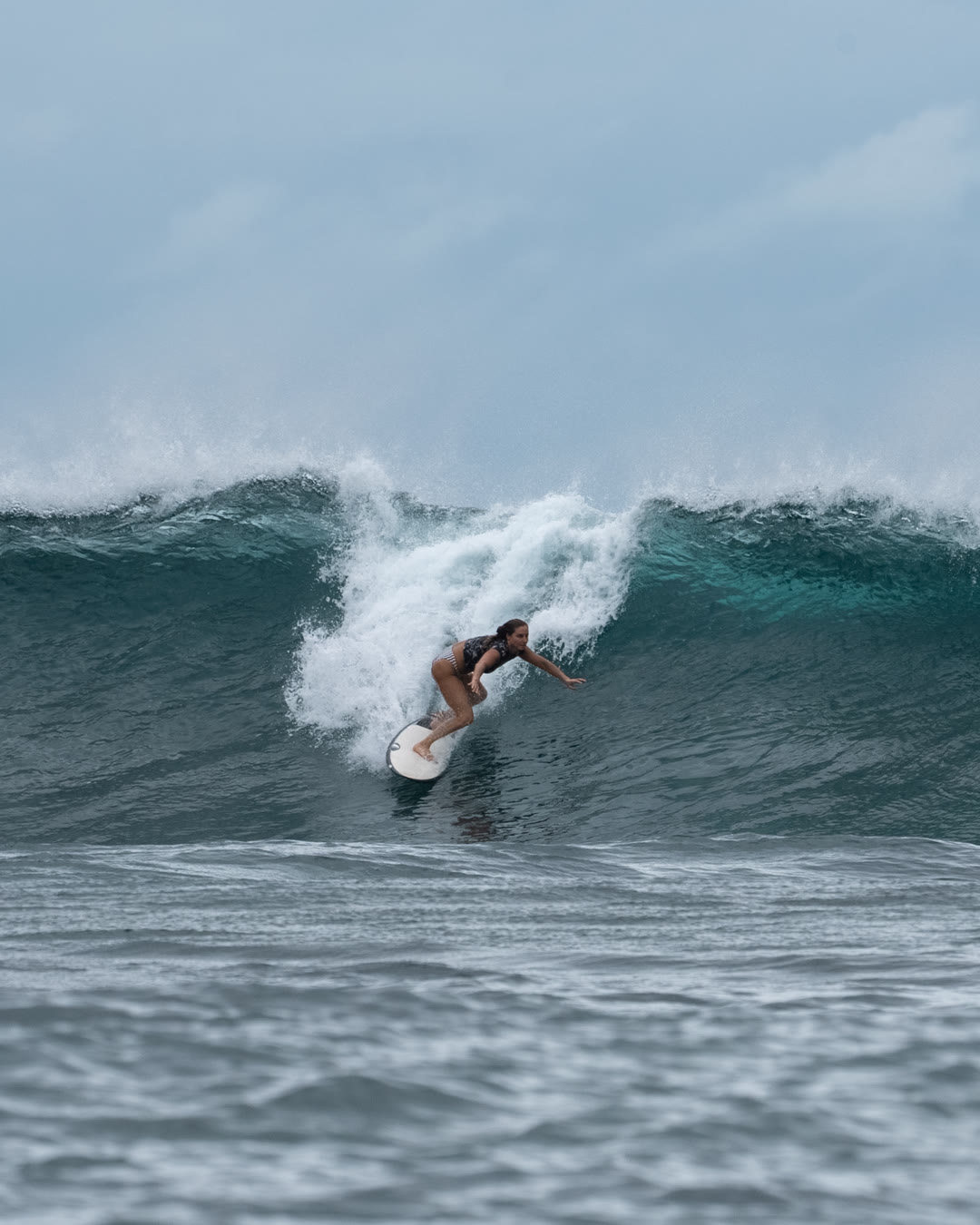 Falyn surfing a reef wave in Indonesia, low on a white board with one hand trailing the face