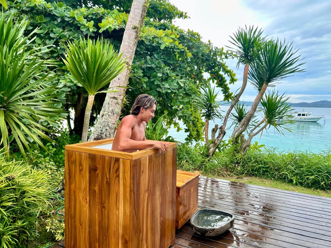 A guest in a teak ice bath on a deck overlooking the ocean