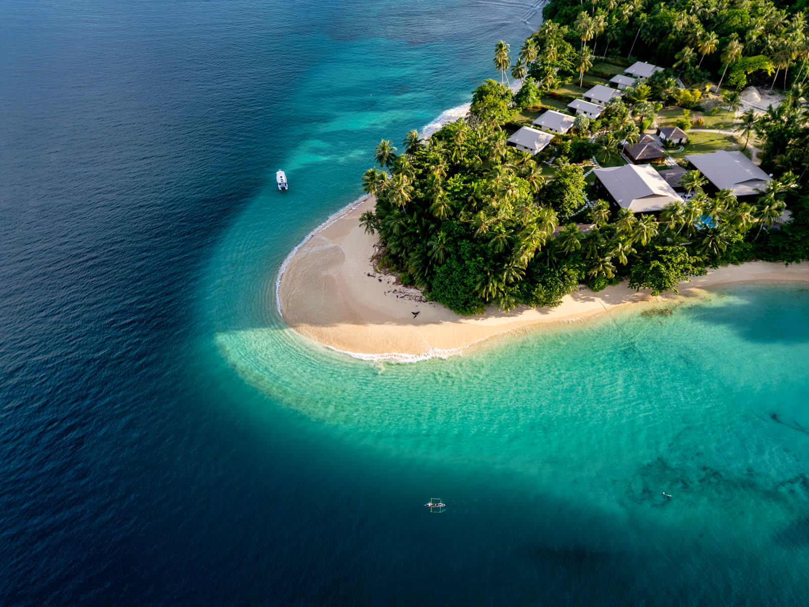 A white sandbar curving off a jungle island into shallow turquoise water